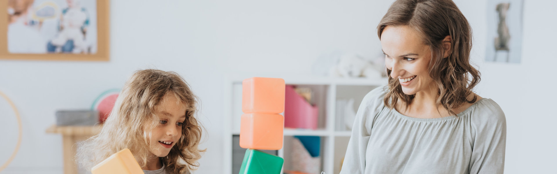 a woman smiling at a little girl playing toy blocks